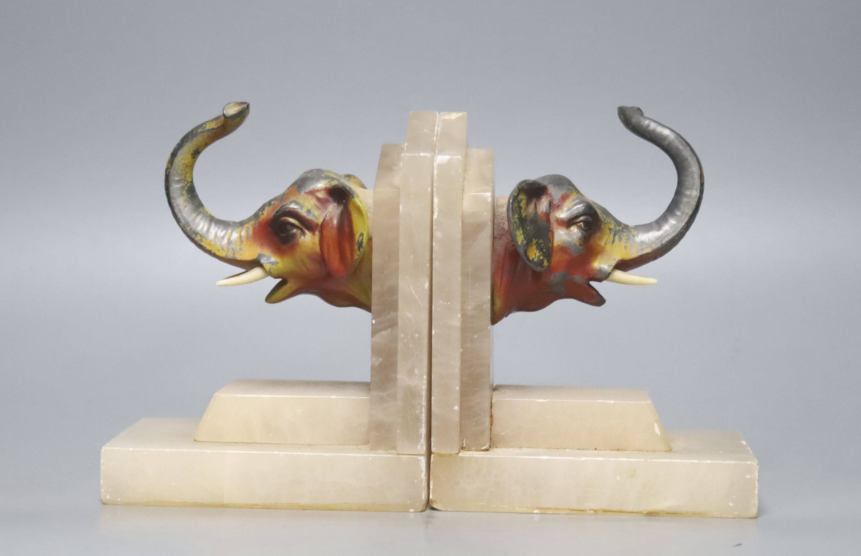 A pair of 1930's alabaster book ends, each applied with a painted metal elephant head, 14cm